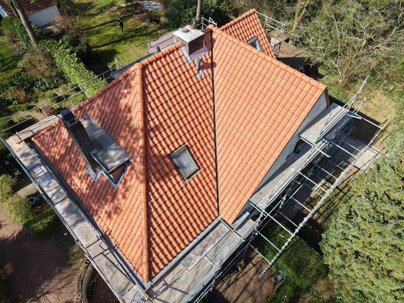 Luchtfoto van huis tijdens dakrenovatie met nieuwe rode dakpannen en steigers