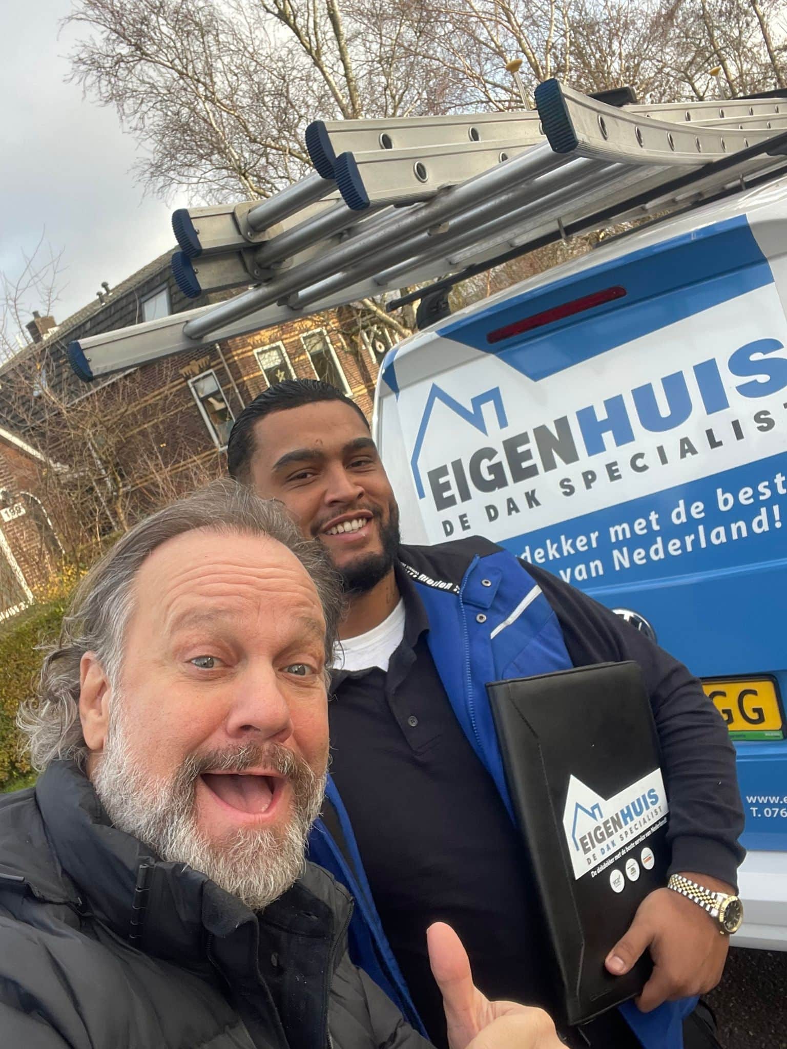 Twee lachende dakspecialisten voor felblauwe Eigenhuis Dak Specialist bus met ladder